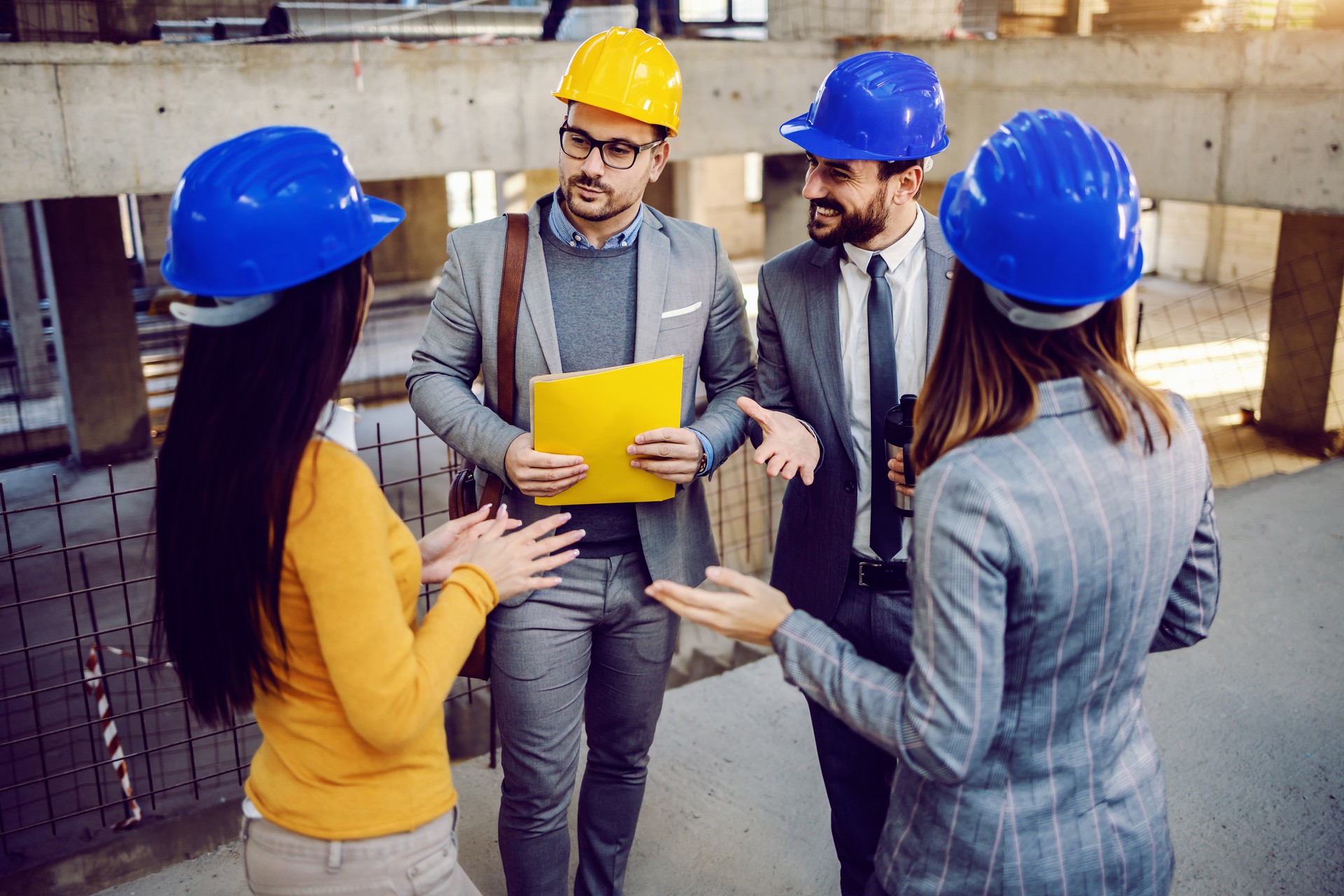 Two female architects telling to their male colleagues ideas how they plan to rebuild building. Men standing and carefully listening to their ideas. Building in construction process interior.